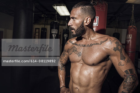 Portrait of tattooed male boxer with hands on hips in gym