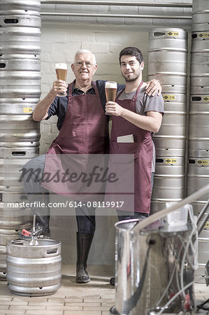 Two brewers drinking beer in the brewery, next to kegs