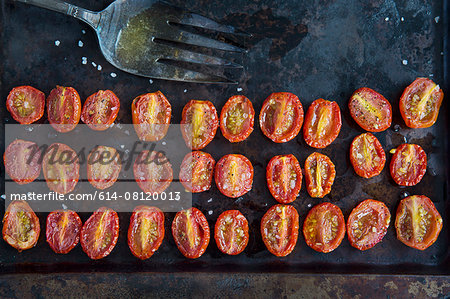 Overhead view of rows of halved roasted tomatoes on baking tin