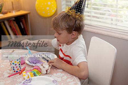 Boy in party hat sitting at table eating birthday cake