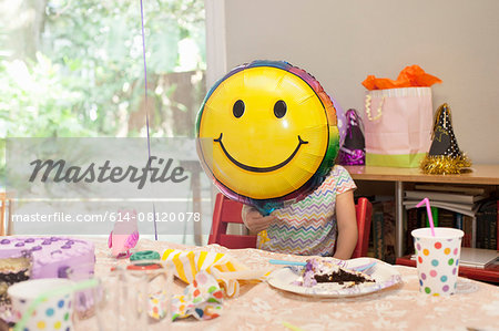 Girl sitting at birthday party table with cake playing with smiley face balloon