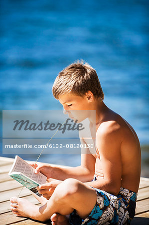 Boy reading book on jetty