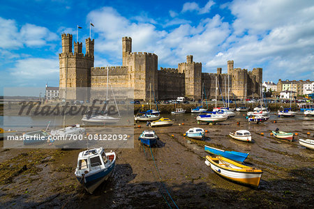 Boats on shore at low tide on River Seiont and Caernarfon Castle, Caernarfon, Gwynedd, Wales, United Kingdom