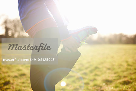 Cropped view of mature female runner stretching leg in field Cropped view of mature female runner stretching leg in field