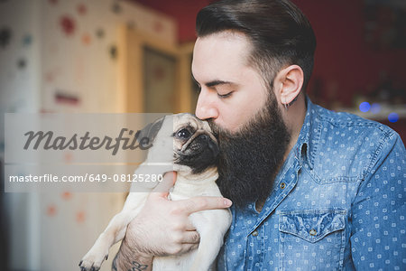 Young bearded man kissing dog in arms Young bearded man kissing dog in arms