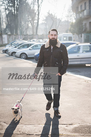 Young bearded man walking dog on street