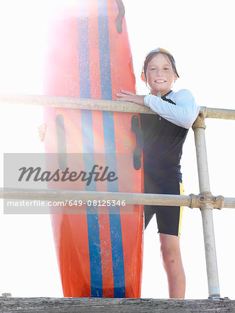 Portrait of boy nipper (child surf life savers) leaning against railings in sunlight, Altona, Melbourne, Australia