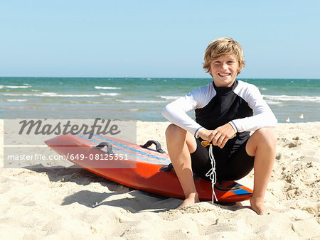 Portrait of confident boy nipper (child surf life savers) sitting on surfboard at beach, Altona, Melbourne, Australia