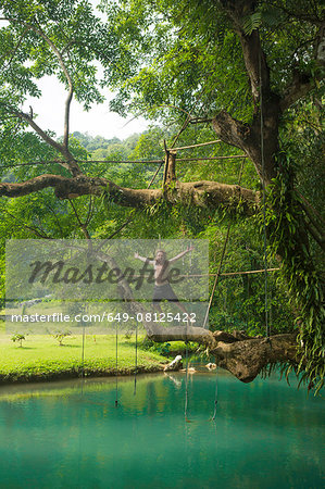 Mature man jumping mid air into turquoise lagoon, Vang Vieng, Laos