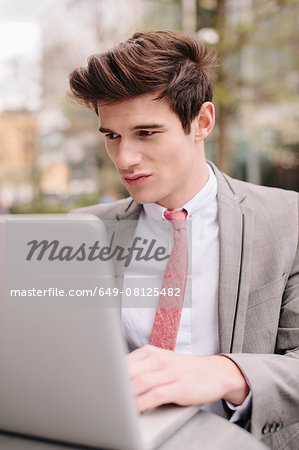 Young city businessman using laptop at sidewalk cafe