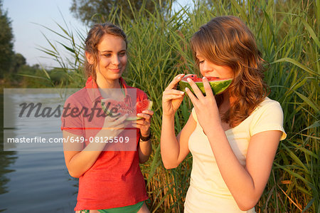 Two young women eating watermelon slices at lakeside