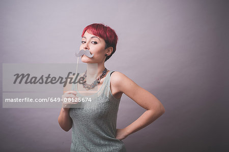 Studio portrait of young woman holding up mustache in front of face