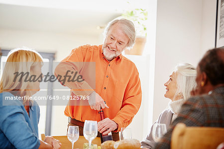 Senior man opening wine with friends