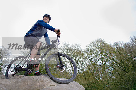 Low angle view of male mountain biker looking out from rock formation