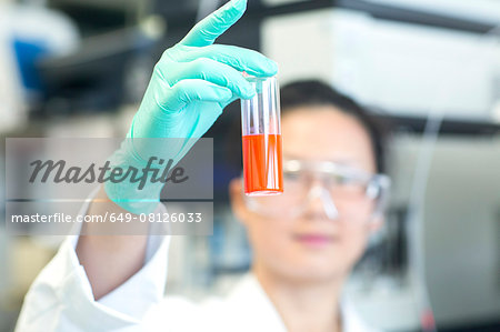 Young female lab technician holding up orange sample in lab Young female lab technician holding up orange sample in lab