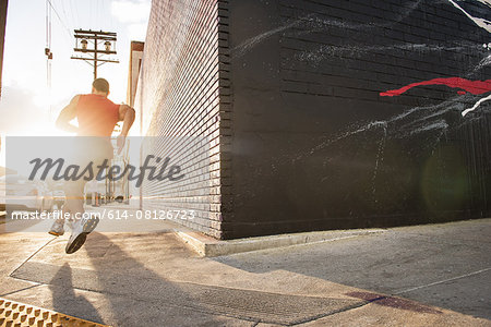 Rear view of male runner running on sidewalk