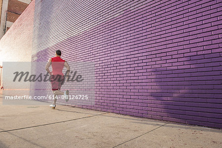 Rear view of male runner running along sidewalk