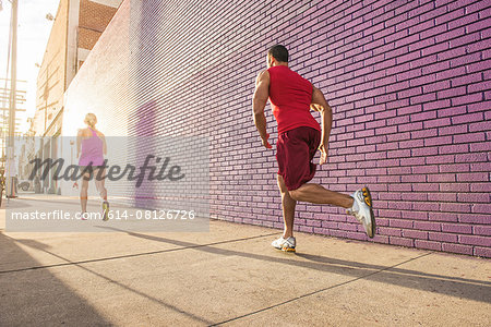 Rear view of male and female runners running along sidewalk Rear view of male and female runners running along sidewalk