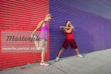 Male and female runners warming up on sidewalk Male and female runners warming up on sidewalk