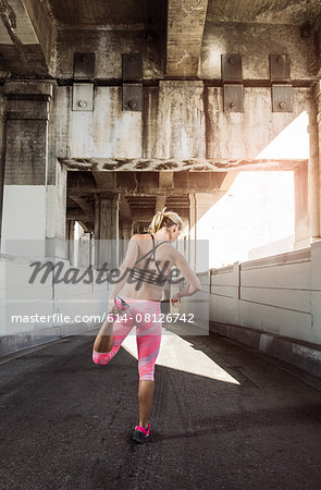 Rear view of female runner warming up under city bridge