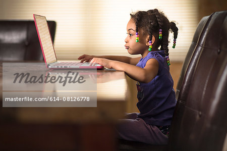 Cute girl at dining table using laptop