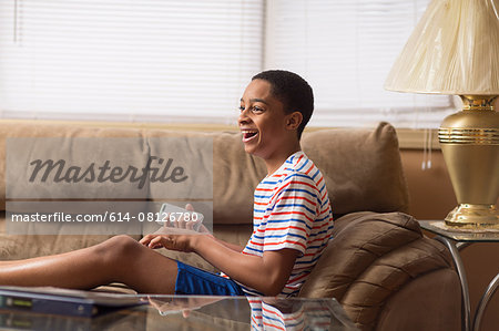 Teenage boy sitting up on sofa laughing