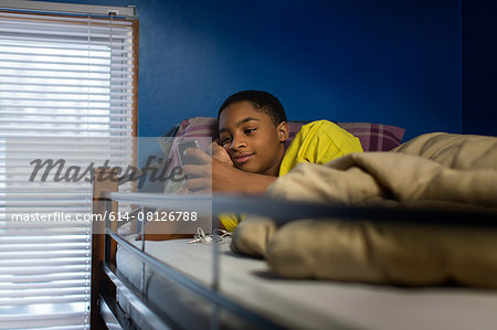 Teenage boy lying in bunkbed reading smartphone text