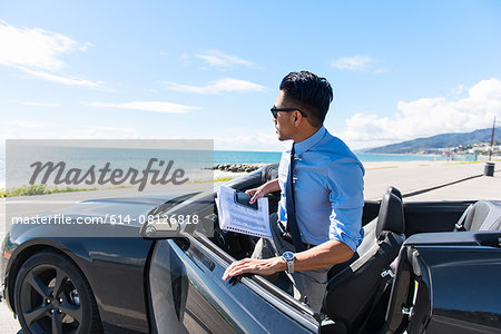 Young businessman getting out of car at coastal parking lot with paperwork