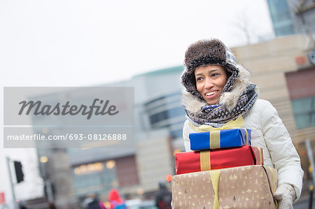 Happy woman looking away while carrying stacked gifts during winter