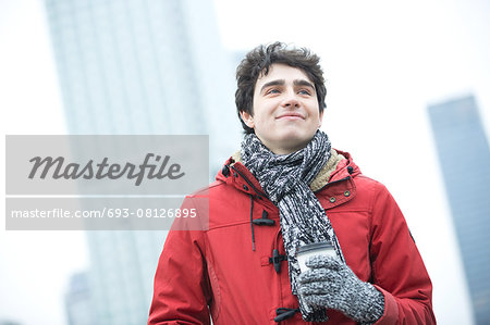 Smiling man in warm clothing looking away while holding disposable cup outdoors