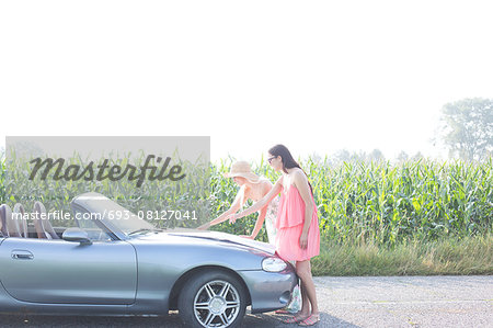Female friends reading map on convertible against clear sky