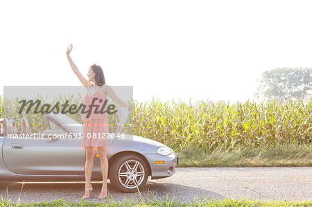 Full length of woman gesturing while holding map by convertible against clear sky