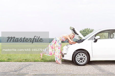 Full-length side view of woman examining broken down car on country road