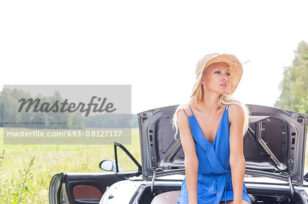 Woman looking away while sitting on convertible trunk against clear sky