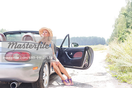 Thoughtful woman sitting in convertible on country road against clear sky