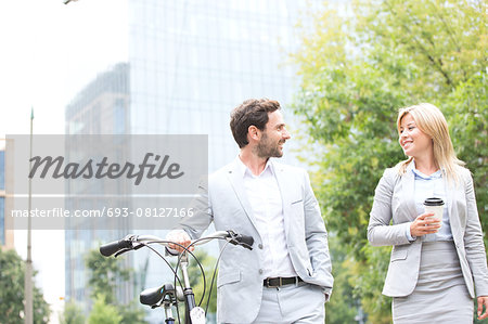 Businesspeople with bicycle and disposable cup conversing while walking outdoors