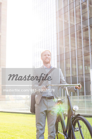 Happy businessman standing with bicycle outside building