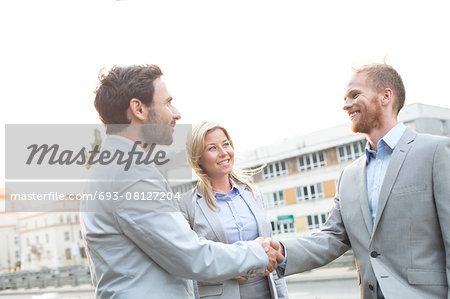 Happy businessmen shaking hands in city against clear sky