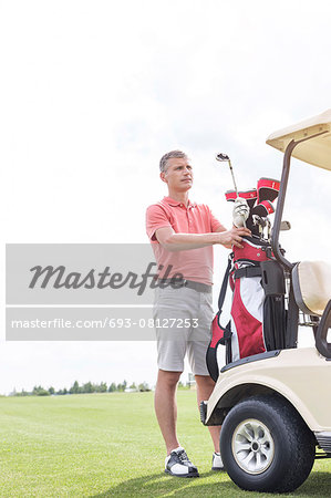 Middle-aged man standing by cart at golf course