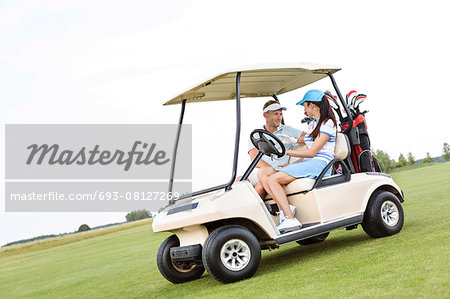 Couple looking at each other while sitting in golf cart against clear sky