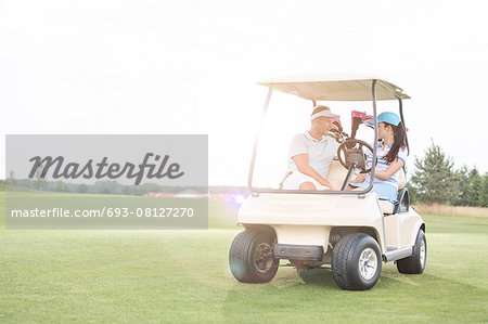 Couple looking at each other while sitting in golf cart against clear sky