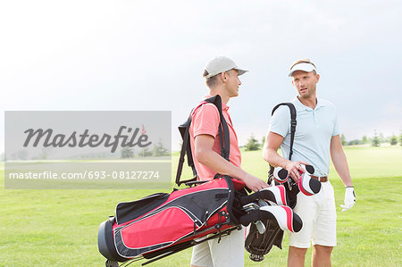 Male golfers communicating at golf course against clear sky