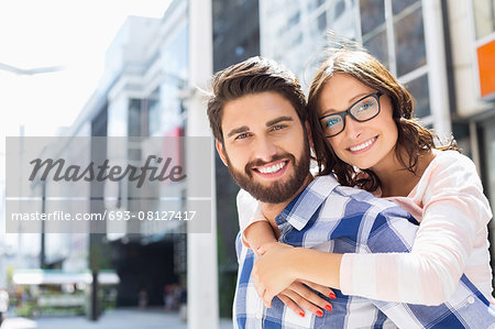 Portrait of happy man giving piggyback ride to woman in city