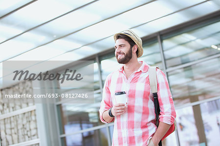Happy man looking away while holding disposable cup in city