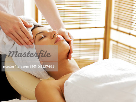 Young woman receiving facial massage, eyes closed