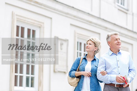 Smiling middle-aged couple standing with arm in arm outside building Smiling middle-aged couple standing with arm in arm outside building