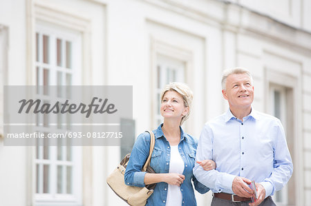 Happy middle-aged couple standing with arm in arm outside building