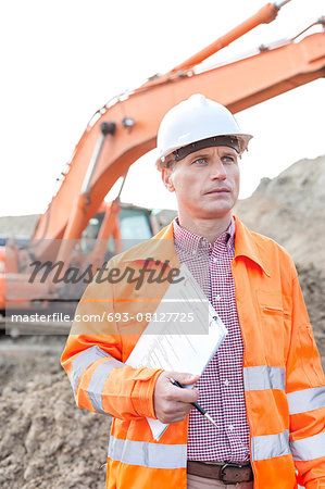 Architect looking away while holding clipboard at construction site