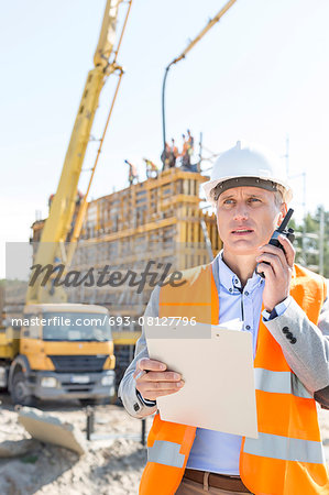 Male supervisor using walkie-talkie while holding clipboard at construction site