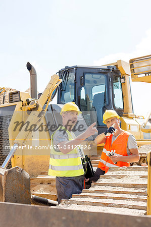 Engineers pointing while discussing at construction site against clear sky